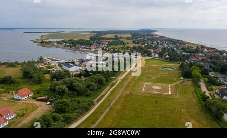 Hiddensee, Germania. 25 Giugno 2021. Vista dell'eliporto (m) e del porto di Vitte (l). Il comune di Seebad Hiddensee sta attualmente progettando l'espansione del porto. Tra le altre cose, si costruisce un nuovo porto turistico con 135 posti barca per imbarcazioni da diporto. Il progetto è controverso. Un'iniziativa dei cittadini sta cercando di impedire il risviluppo del porto. (Vista aerea con drone) Credit: Stephan Schulz/dpa-Zentralbild/ZB/dpa/Alamy Live News Foto Stock