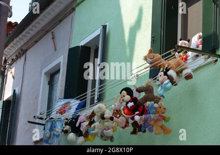 Giocattoli per bambini appesi ad asciugare dalle finestre di una casa colorata a Venezia Foto Stock