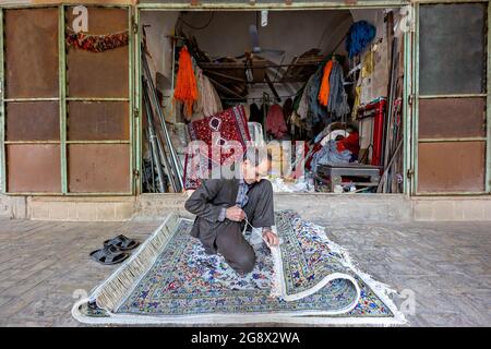 L'uomo locale organizza le frange di tappeto persiano nel bazar a Yazd, Iran Foto Stock