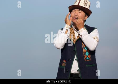 Musicista kirghiso che suona uno strumento musicale tradizionale conosciuto come Timur Komuz, una versione dell'arpa della mandibola, a Issyk Kul, Kirghizistan Foto Stock