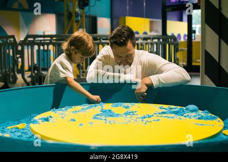 Ragazzo e suo padre stanno giocando con entusiasmo con la sabbia cinetica colorata nel centro di gioco. Terapia di sabbia. Creatività e relax. Amore parentale e. Foto Stock