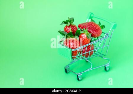 Fragole fresche e deliziose in un carrello su sfondo verde pastello, concetto di shopping Foto Stock