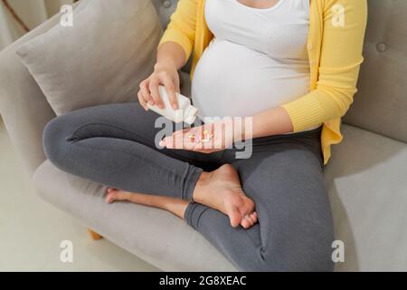 donna incinta che versa pillole in mano dalla bottiglia a casa Foto Stock