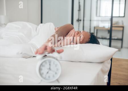 Giovane donna dalla pelle scura sdraiata a letto e che spegne l'allarme Foto Stock