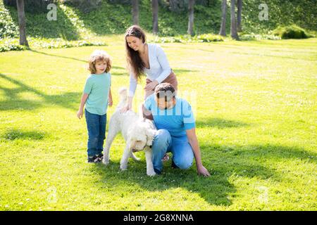 felice famiglia di papà madre e figlio di capretto che gioca con cane animale domestico in estate parco verde erba, relax Foto Stock