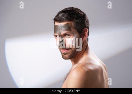 Uomo che usa i prodotti del viso sulla sua pelle. Trattamenti con maschera facciale. Ringiovanimento, aggiunta di umidità maschere. Foto Stock