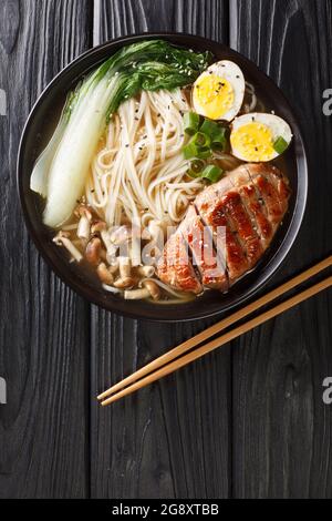 Tagliatelle asiatiche di Miso Ramen con uovo, anatra e cavolo di pak Choi in ciotola su fondo scuro closeup. Vista dall'alto verticale Foto Stock