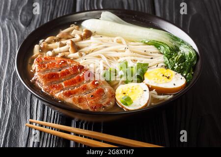 Zuppa asiatica di noodle, ramen con anatra, funghi, verdure e uova in ciotola su fondo di legno nero. Orizzontale Foto Stock