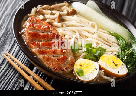 Ramen giapponese fatto in casa con anatra, funghi, uova e cavolo di pak choi in ciotola su tavola nera primo piano. Orizzontale Foto Stock