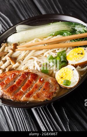 Ramen con anatra, funghi, uova e bok choy primo piano in una ciotola sul tavolo. Verticale Foto Stock