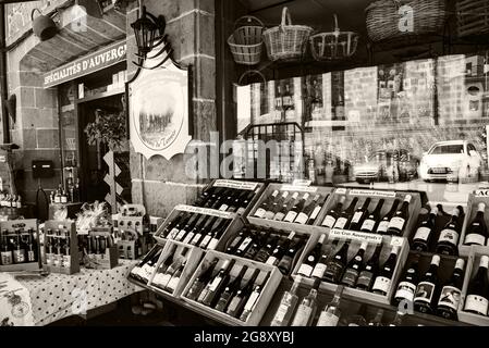 Besse, Francia - 30 maggio 2021: All'aperto di cibo locale e negozio di specialità del vino nella città medievale in Auvergne. Strada riflessa nella finestra di visualizzazione. Seppia Foto Stock