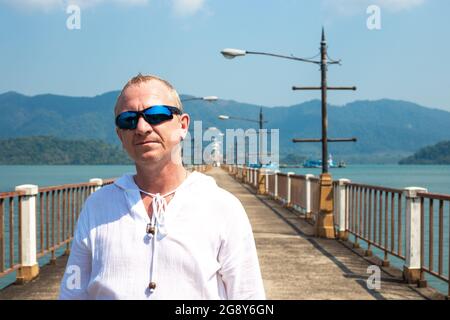 uomo biondo maturo su un molo in mare in asia Foto Stock