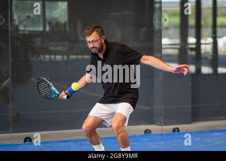 Uomo che gioca a un padel in un campo di erba blu al coperto - giovane sportivo ragazzo padel giocatore che colpisce palla con una racchetta Foto Stock