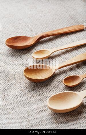 Cucchiai artigianali fatti da diversi tipi di legno giacciono in fila su un tessuto di tela di canapa Foto Stock