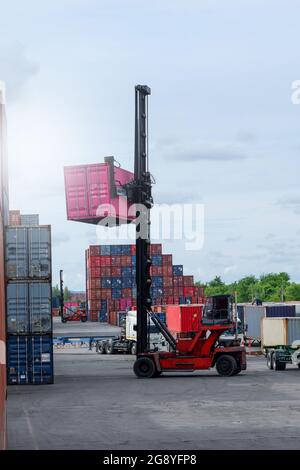 Carrello elevatore a forche di sollevamento del contenitore di carico in cantiere per la spedizione o la dock yard contro Alba cielo con un contenitore di carico in pila in background per i mezzi di trasporto Foto Stock