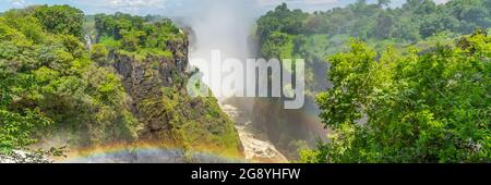 Rainbow sopra le Cascate Victoria sul Fiume Zambesi, confine dello Zambia e vista panoramica dello Zimbabwe con cielo blu Foto Stock