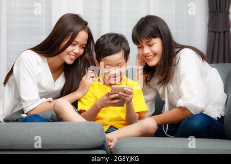 Tre bambini della famiglia asiatica, un ragazzo e due ragazze giocano a casa con la felicità, utilizzando lo smartphone per ascoltare musica e guardare video Foto Stock