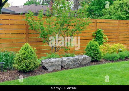 Questo giardino di ispirazione Asiatica e splendidamente mantenuto presenta una recinzione in cedro dallo stile minimalista con tavole orizzontali. Foto Stock