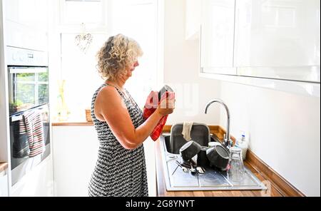 Donna che fa su i piatti in cucina luminosa illuminata nelle faccende domestiche di luce del giorno Foto Stock