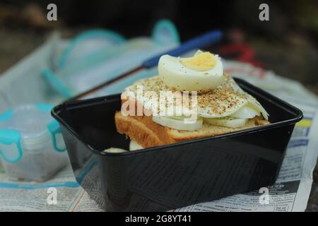 Sandwich di formaggio all'uovo, confezionato all'interno di una scatola di plastica nera. Facile da preparare per il trekking se sono disponibili pane, uova sode, formaggio, sale e pepe. Foto Stock