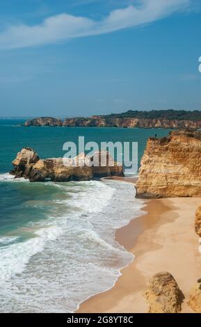 Vista verticale della bellissima spiaggia con scogliere e onde lunghe, cielo blu con nuvole rare, acque blu profonde - spazio per il testo Foto Stock