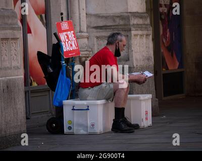 Big Issue seller with We're Back Sign in Bishopsgate London, durante il Covid-19, Covid, pandemia di coronavirus, la Big Issue è una delle principali imprese sociali del Regno Unito e aiuta le persone senza casa, o persone a rischio di homelessness, l'opportunità di guadagnare un salario Foto Stock