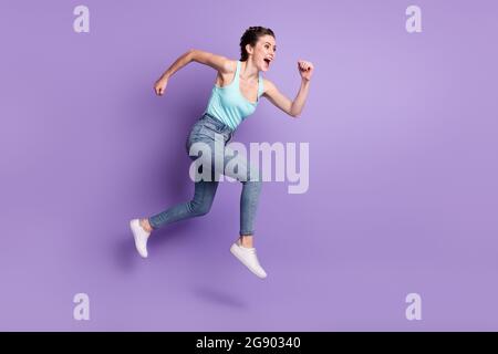 Lunghezza intera dimensione del corpo profilo vista laterale di bella ragazza allegra saltando corsa isolata su sfondo viola di colore viola Foto Stock