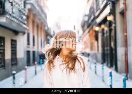 Felice giovane donna che canta i capelli mentre si alza in piedi al vicolo Foto Stock