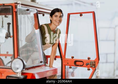 Sorridente giovane agricoltore in piedi alla porta del trattore Foto Stock