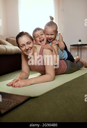 Ragazzo allegro e ragazza sdraiata sulla madre che si esercita nel soggiorno Foto Stock
