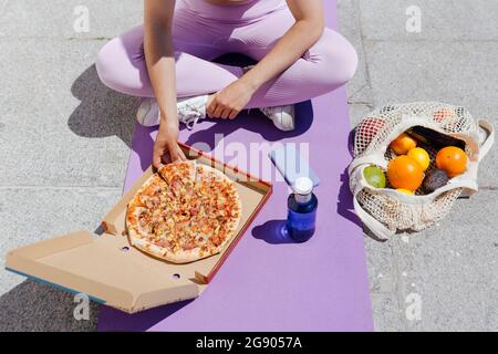 Sportswoman che ha la pizza mentre si siede a gambe incrociate su materassino di esercitazione Foto Stock