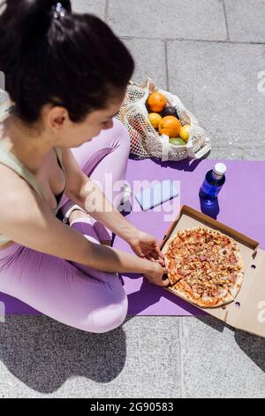 Atleta femminile che ha la pizza sul tappeto da allenamento durante la giornata di sole Foto Stock