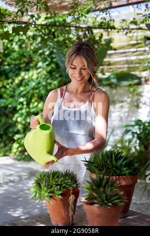 Donna sorridente innaffiare le piante mentre si trova in piedi in cortile Foto Stock