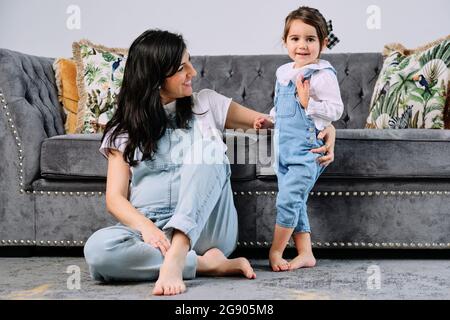 Donna incinta sorridente con figlia carina in soggiorno a casa Foto Stock