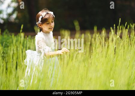 Ragazza in abito bianco che tocca l'erba nel suo giorno di comunione Foto Stock