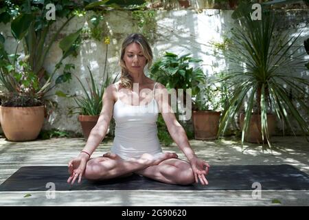 Donna matura meditating in loto posizionando su tappeto di esercitazione Foto Stock
