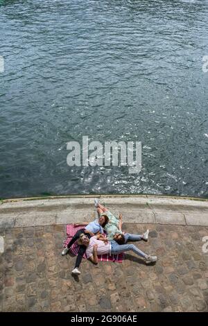 Amici maschi e femmine che giacciono sul lungomare lungo il fiume Foto Stock