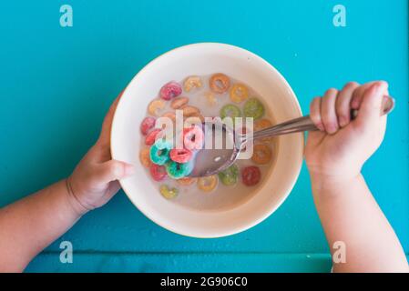 Ragazza che tiene il cucchiaio riempito di cereali e latte sul tavolo Foto Stock