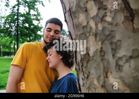 Giovane coppia con occhi chiusi in piedi insieme da un tronco d'albero al parco Foto Stock