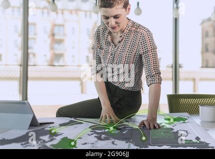 Professionista femminile che guarda i dati di comunicazione sulla mappa alla scrivania in ufficio Foto Stock