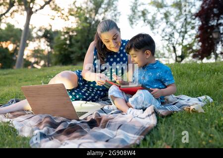 Eccitata donna che assiste ragazzo lettura libro di storia nel parco pubblico Foto Stock