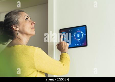 Donna che guarda lontano mentre si trova accanto a un dispositivo di automazione a parete Foto Stock