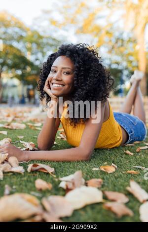 Giovane donna felice con capelli ricci adagiati sull'erba del parco Foto Stock