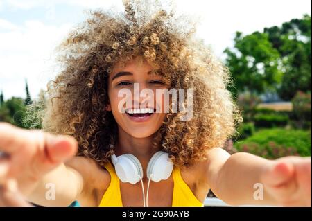 Donna allegra con capelli ricci che indossa le cuffie il giorno di sole Foto Stock