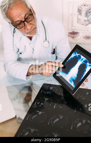 Medico senior maschile che spiega l'immagine radiografica digitale su tablet in ospedale Foto Stock