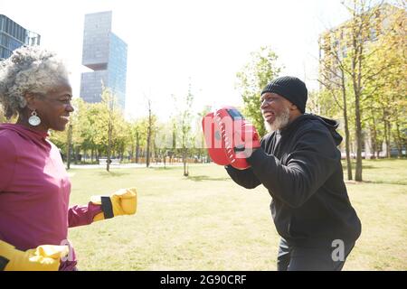 Donna sorridente che pratica pugilato con l'uomo al parco Foto Stock