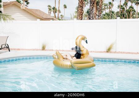 Donna che si rilassa su un cigno gonfiabile in piscina Foto Stock