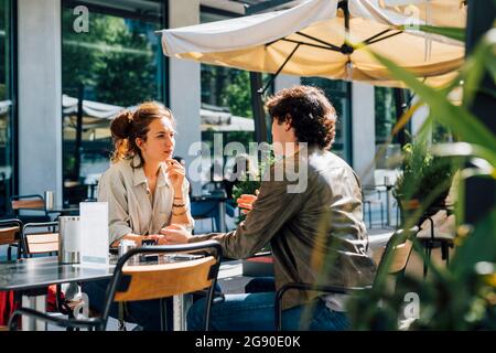 La coppia parla mentre sii al caffè sul marciapiede durante la giornata di sole Foto Stock