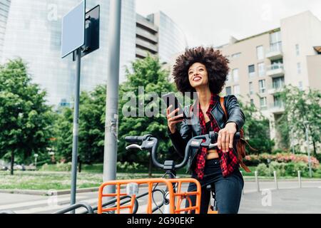 Giovane donna che sblockano la bicicletta con lo smartphone presso la stazione di parcheggio Foto Stock