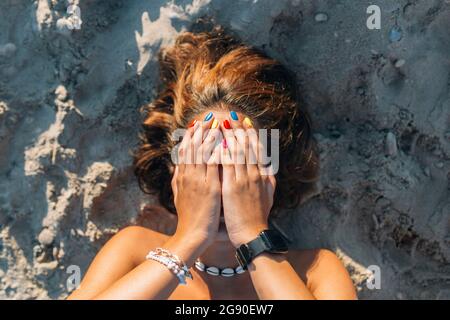 Donna che ricopre il viso con le mani mentre si trova sulla sabbia durante la giornata di sole Foto Stock